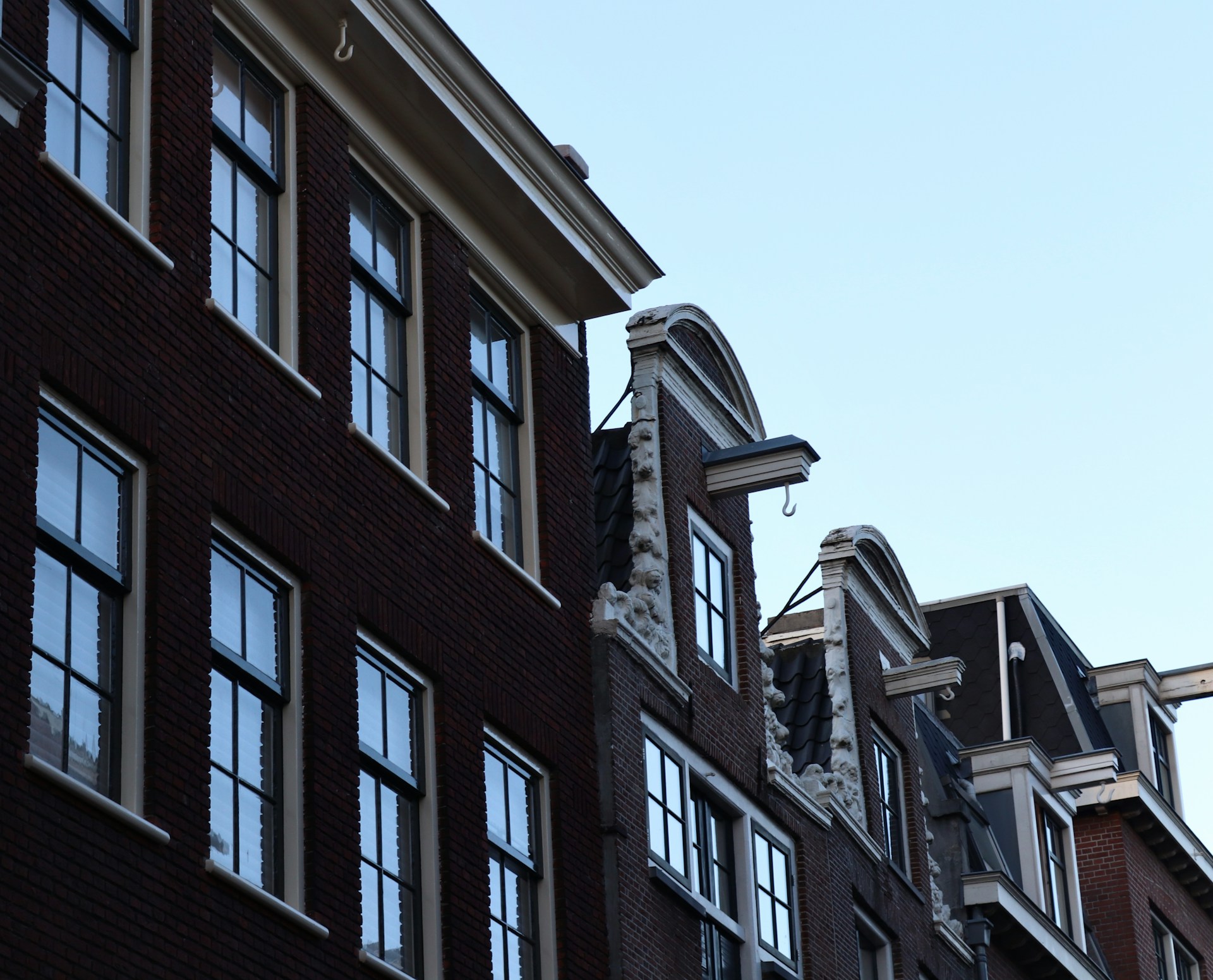 Close-up view of traditional Dutch canal house facades with large windows and decorative gables against a clear sky.