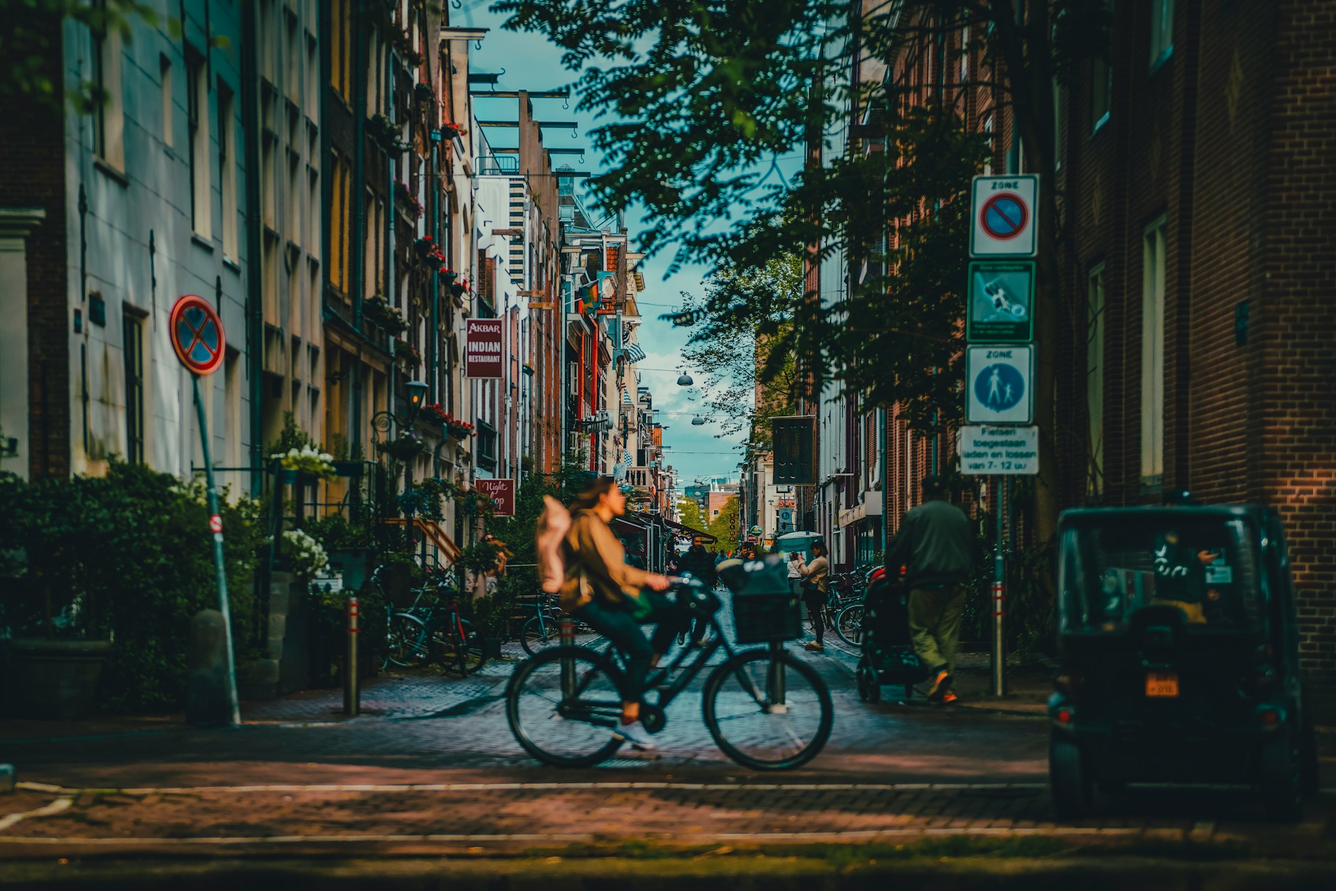 Blurred cyclist riding on a narrow cobblestone street lined with brick buildings and pedestrians in an urban setting.