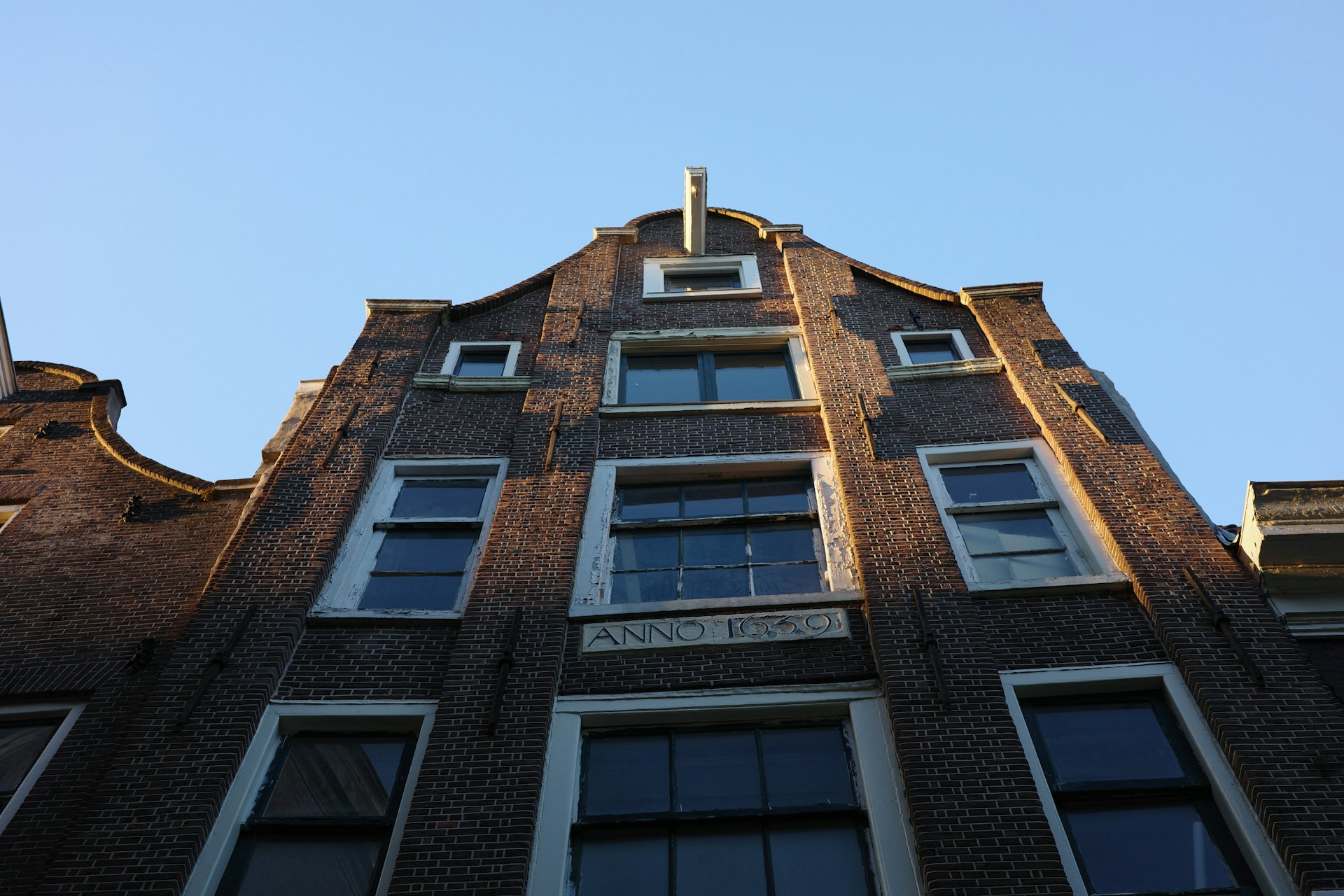 Low-angle view of a historic brick building facade with multiple windows and a plaque stating 'Anno 1639' against a clear blue sky.